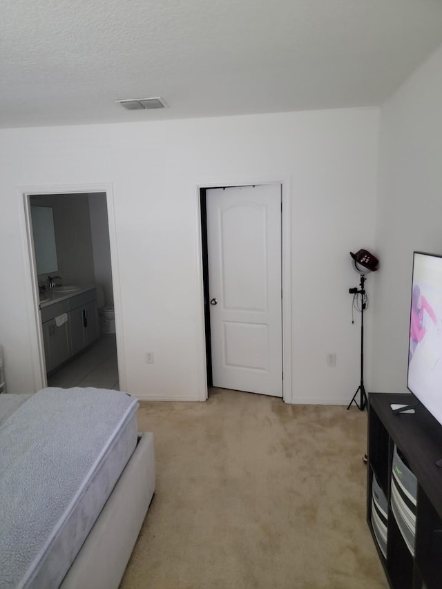 bedroom featuring ensuite bath, light carpet, and sink