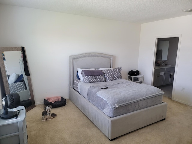 bedroom featuring sink, ensuite bathroom, light carpet, and a textured ceiling