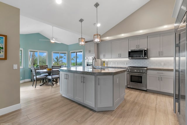 kitchen with a kitchen island with sink, light wood-type flooring, stainless steel appliances, gray cabinets, and decorative light fixtures