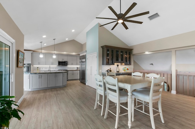 dining space featuring sink, ceiling fan, high vaulted ceiling, and light hardwood / wood-style flooring