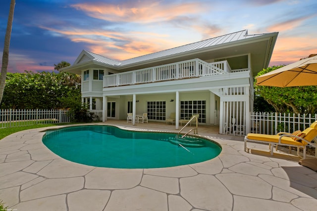 back house at dusk with a patio, a fenced in pool, and a balcony