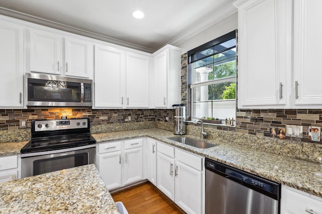 kitchen featuring appliances with stainless steel finishes, a sink, ornamental molding, white cabinets, and tasteful backsplash