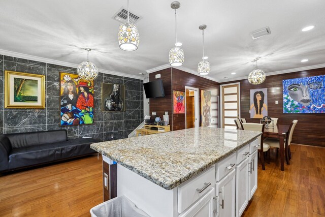 kitchen with a kitchen island, crown molding, hanging light fixtures, hardwood / wood-style flooring, and white cabinets