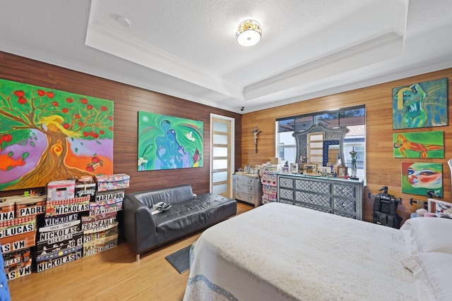 bedroom featuring a raised ceiling, wooden walls, wood finished floors, a textured ceiling, and crown molding