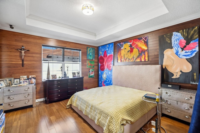 bedroom with a textured ceiling, hardwood / wood-style floors, a raised ceiling, wood walls, and ornamental molding