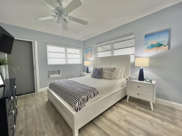 bedroom with light wood-type flooring, a wall unit AC, and baseboards