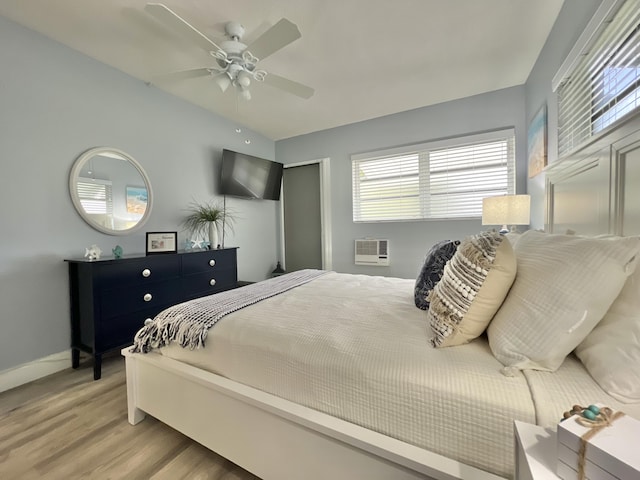 bedroom with a wall mounted air conditioner, baseboards, ceiling fan, and light wood finished floors