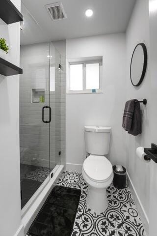 bathroom with tile patterned floors, toilet, and a shower with shower door