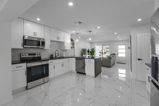 kitchen with tasteful backsplash, hanging light fixtures, stainless steel appliances, kitchen peninsula, and white cabinetry