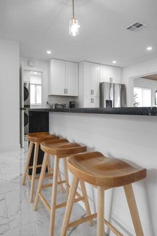 kitchen with stacked washer / drying machine, plenty of natural light, stainless steel refrigerator, and white cabinets