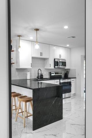 kitchen with white cabinets, decorative light fixtures, appliances with stainless steel finishes, sink, and a breakfast bar