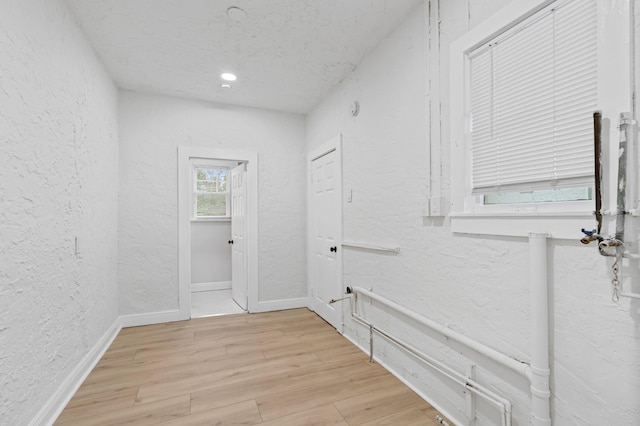 hall with light wood-type flooring and a textured ceiling