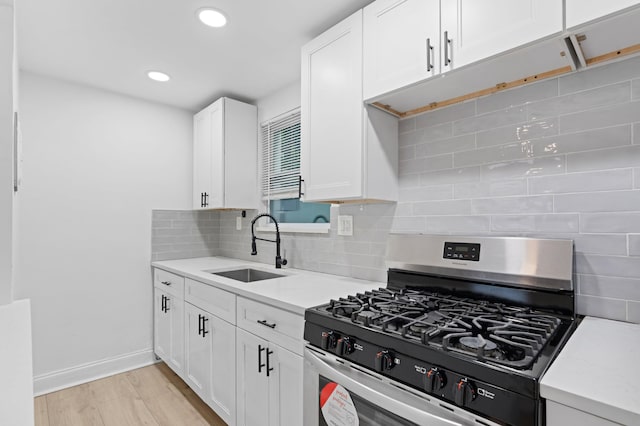 kitchen with light hardwood / wood-style flooring, white cabinetry, sink, stainless steel range with gas cooktop, and tasteful backsplash