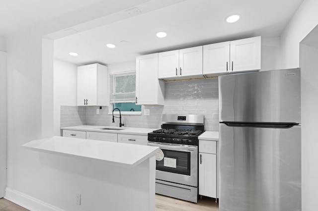 kitchen featuring appliances with stainless steel finishes, sink, decorative backsplash, white cabinetry, and light wood-type flooring