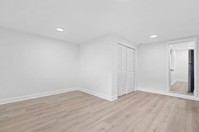 unfurnished bedroom with a closet, stainless steel refrigerator, and light hardwood / wood-style flooring