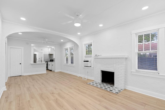 unfurnished living room featuring light hardwood / wood-style flooring, ceiling fan, ornamental molding, and a fireplace