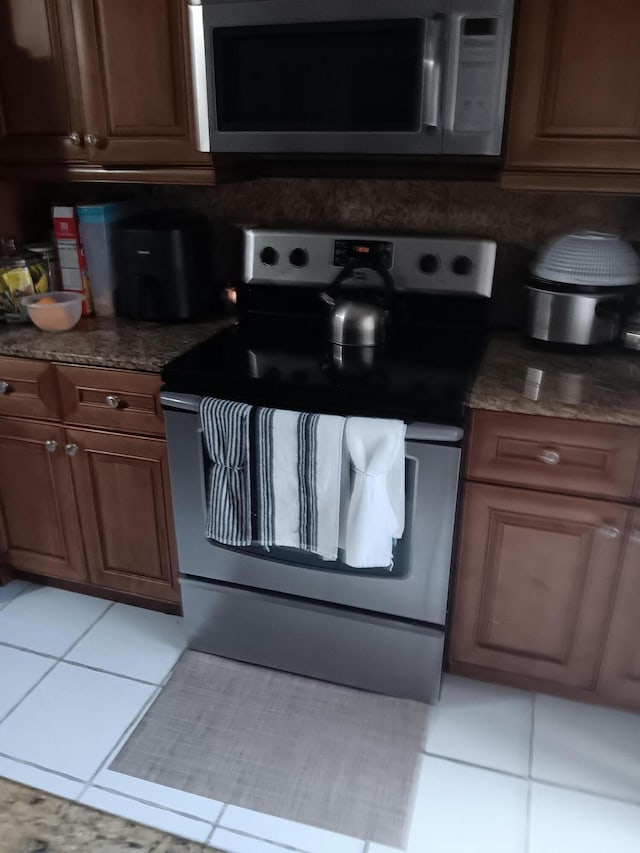 kitchen featuring appliances with stainless steel finishes, dark stone countertops, and light tile patterned floors