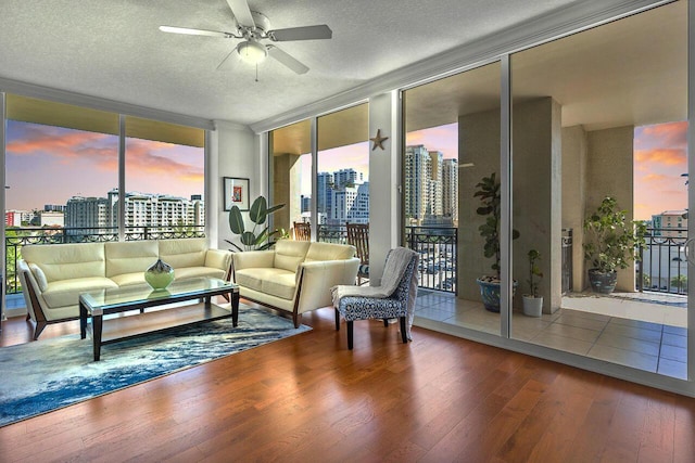 living room featuring ceiling fan, wood-type flooring, expansive windows, and a textured ceiling