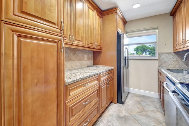 kitchen with tasteful backsplash, sink, light tile patterned floors, light stone countertops, and stainless steel fridge