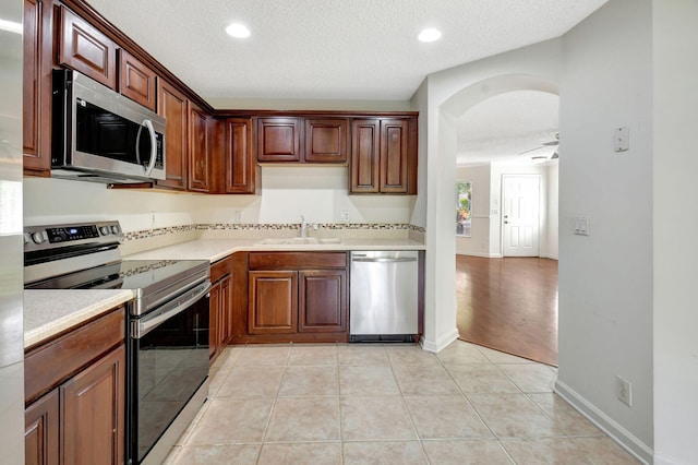 kitchen with appliances with stainless steel finishes, a textured ceiling, sink, and light tile patterned floors