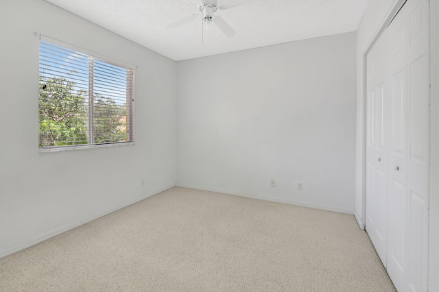 unfurnished bedroom with a textured ceiling, ceiling fan, light colored carpet, and a closet