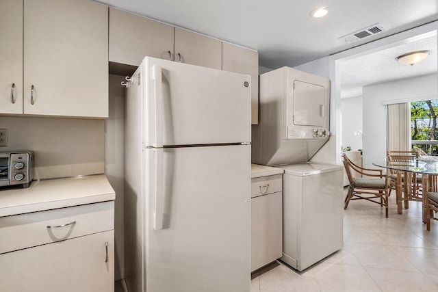 kitchen with white refrigerator, light tile patterned floors, a textured ceiling, and stacked washer / dryer