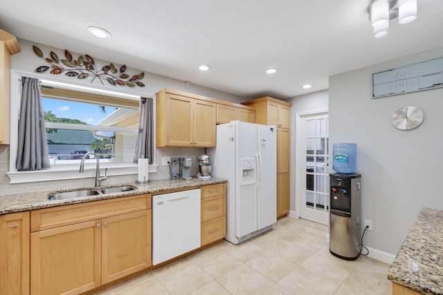 kitchen with white appliances, light brown cabinets, light stone counters, and sink