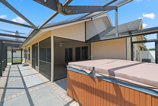 rear view of house with a hot tub, glass enclosure, ceiling fan, and a patio