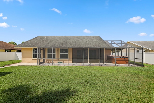 rear view of property with a hot tub, glass enclosure, a patio area, and a yard