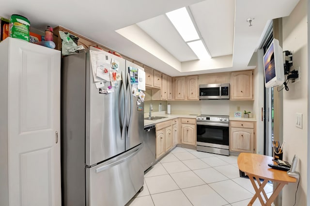 kitchen featuring light tile patterned floors, sink, appliances with stainless steel finishes, a tray ceiling, and light brown cabinetry