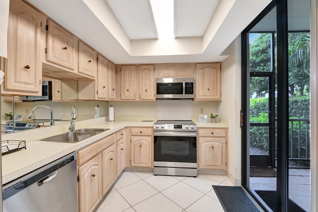 kitchen with appliances with stainless steel finishes, a raised ceiling, light tile patterned floors, light brown cabinetry, and sink