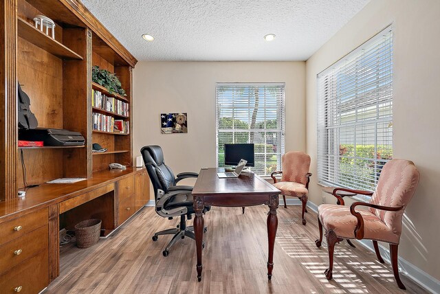 office area with a textured ceiling, light wood-type flooring, and a wealth of natural light