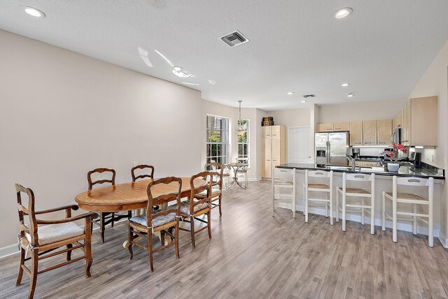 dining area with a textured ceiling, light wood-type flooring, and sink