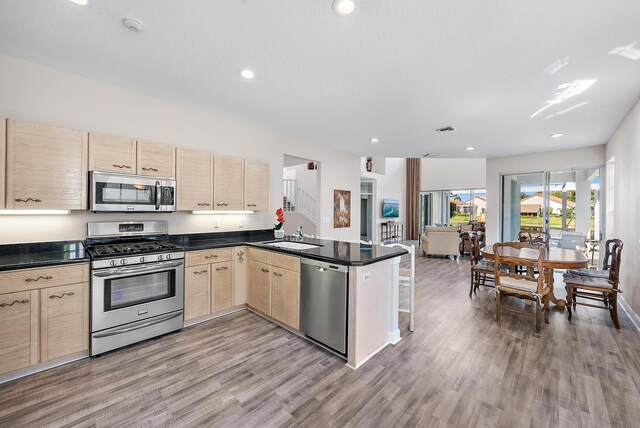 kitchen with appliances with stainless steel finishes, wood-type flooring, kitchen peninsula, and light brown cabinetry