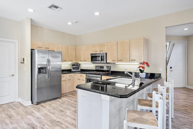 kitchen featuring light hardwood / wood-style floors, a breakfast bar area, kitchen peninsula, stainless steel appliances, and light brown cabinets