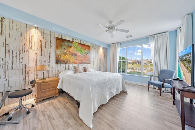 bedroom featuring light hardwood / wood-style floors, wooden walls, and ceiling fan