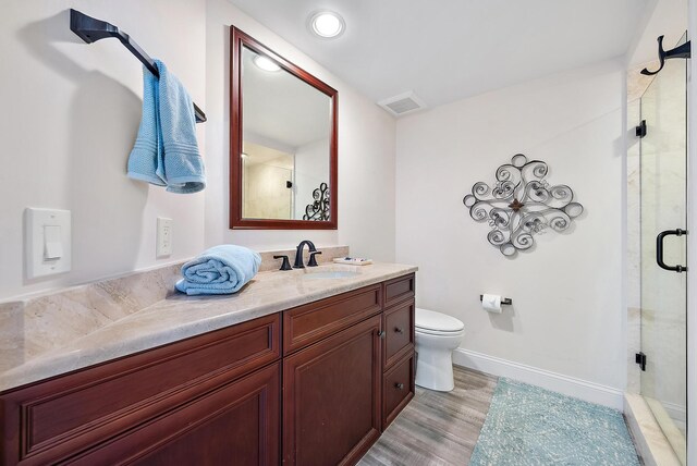 bathroom featuring wood-type flooring, vanity, a shower with shower door, and toilet