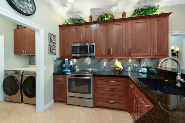 kitchen with washing machine and clothes dryer, stainless steel appliances, ornamental molding, a sink, and dark stone counters