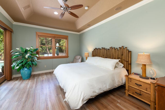 bedroom featuring a ceiling fan, baseboards, ornamental molding, light wood-type flooring, and a tray ceiling