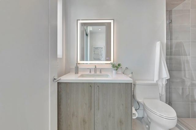 bathroom with tiled shower, vanity, and toilet