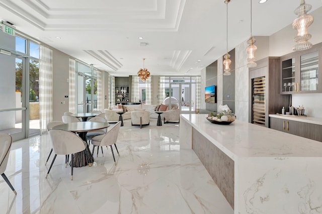 kitchen featuring a tray ceiling, an inviting chandelier, decorative light fixtures, light stone countertops, and french doors