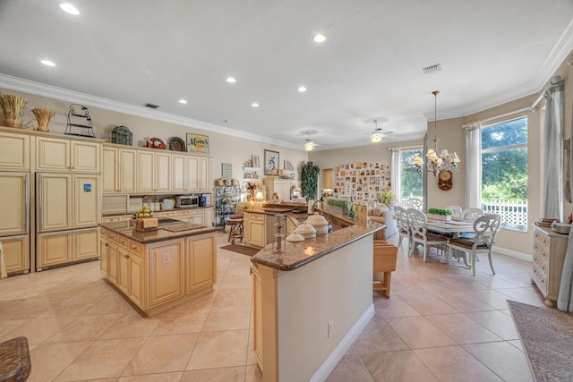 kitchen with cream cabinets, hanging light fixtures, an island with sink, dark stone counters, and ornamental molding