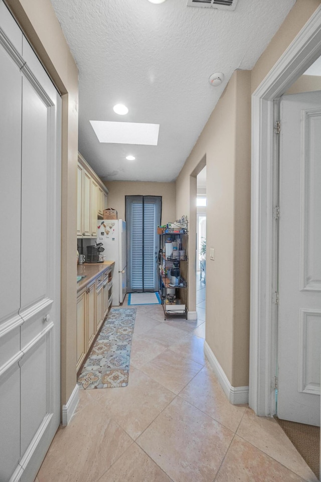 kitchen featuring cream cabinets, a textured ceiling, light tile patterned flooring, a skylight, and white fridge