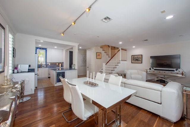 dining room featuring rail lighting, crown molding, beverage cooler, dark hardwood / wood-style floors, and sink