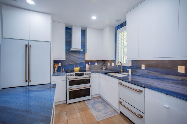 kitchen with wall chimney exhaust hood, white appliances, white cabinetry, and sink