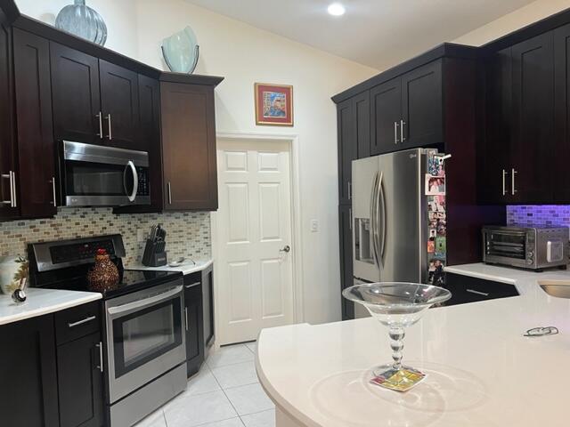 kitchen with appliances with stainless steel finishes, vaulted ceiling, backsplash, and light tile patterned flooring