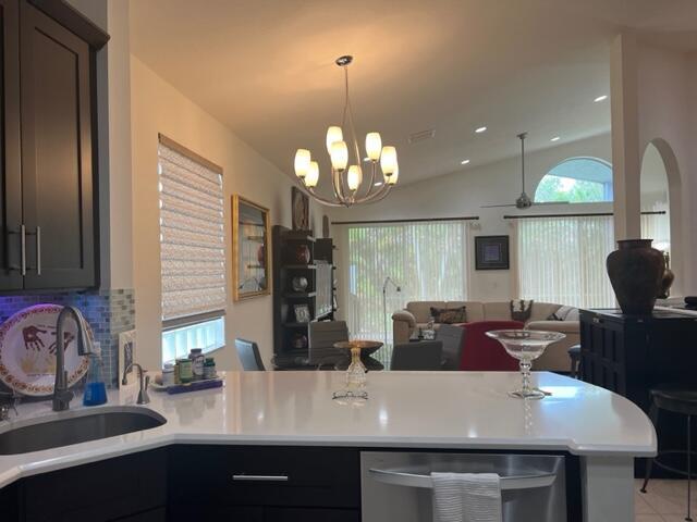 kitchen with kitchen peninsula, an inviting chandelier, sink, decorative backsplash, and vaulted ceiling