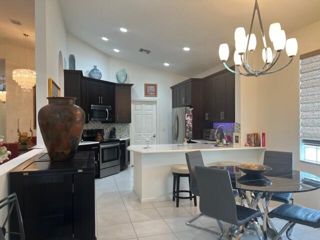 kitchen featuring a notable chandelier, a kitchen bar, kitchen peninsula, appliances with stainless steel finishes, and lofted ceiling