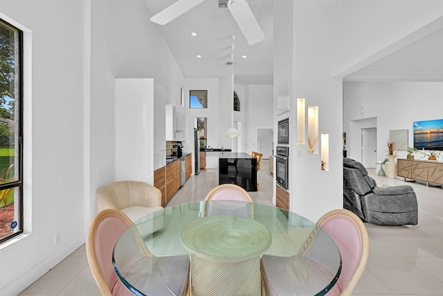 dining space with a towering ceiling, ceiling fan, and light tile patterned floors