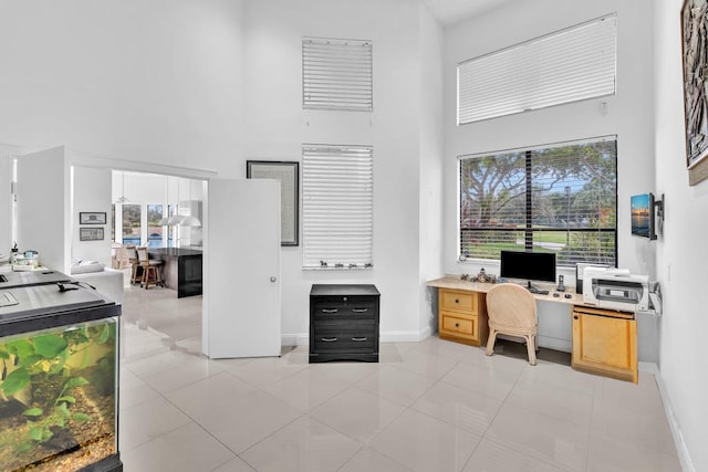 home office with built in desk, a towering ceiling, and light tile patterned floors